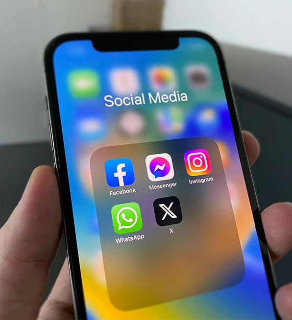 A hand holds an iPhone showing a "Social Media" app folder with icons for Facebook, Messenger, Instagram, WhatsApp, and X, highlighting digital marketing services.